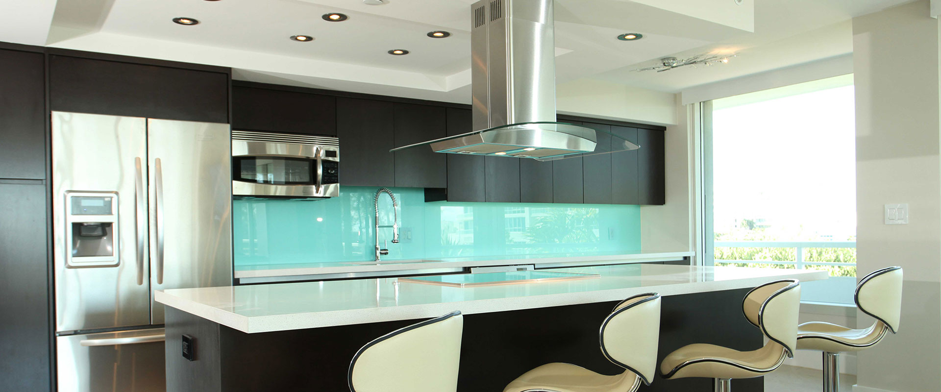 A modern kitchen with a a large center island. The back bench as a vibrant aquamarine coloured glass splashback